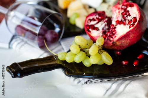 Fototapeta Naklejka Na Ścianę i Meble -  Cheese platter with different cheese and grapes, served on a glass transparent dish from a melted bottle