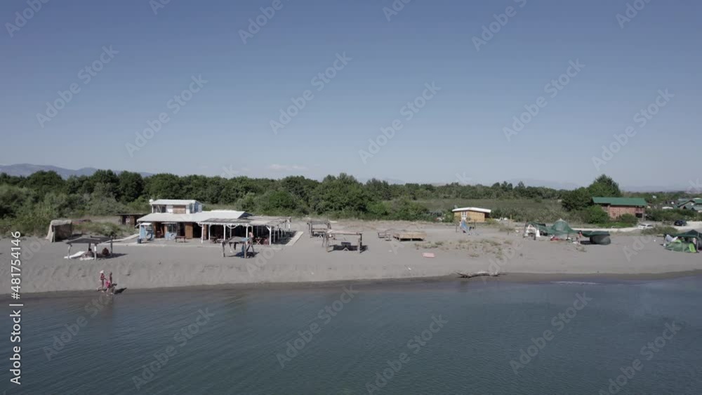 drone video on the shore of Nomada beach in motenegro with people walking ending up in the bojana river, cabins and a beach bar are seen, drone video on the shore of Nomada beach in motenegro with people walking ending up in the bojana river, cabins and a beach bar are seen,