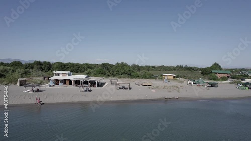 drone video on the shore of Nomada beach in motenegro with people walking ending up in the bojana river, cabins and a beach bar are seen, 