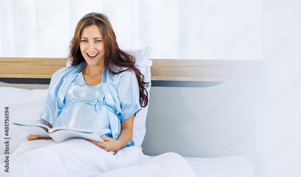 Beautiful pregnant woman on pajamas resting on bed with smile and happy to read book for prenatal care of maternity Beautiful pregnant woman on pajamas resting on bed with smile and happy to read book for prenatal care of maternity