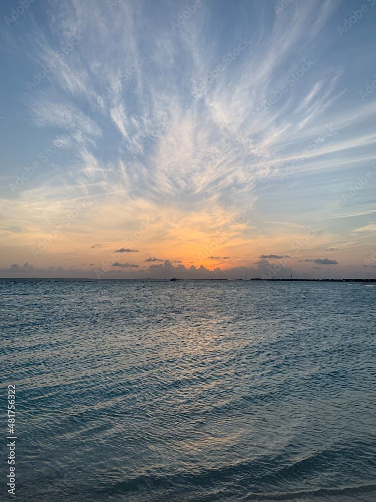 Dawn in the Maldives, the sun rises from behind the clouds, illuminating the very beautiful clouds and water of the Indian Ocean