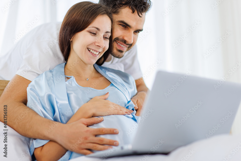 Lovely pregnant wife tenderly touch beloved belly of unborn baby while lounging on bed with smile and happy as enjoy watching entertainment media on computer Lovely pregnant wife tenderly touch beloved belly of unborn baby while lounging on bed with smile and happy as enjoy watching entertainment media on computer