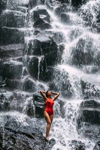 Beautiful girl at a waterfall on the island of Bali Indonesia. Sexy girl at the waterfall. Young and beautiful girl in bikini taking bath in a waterfall. Copy space