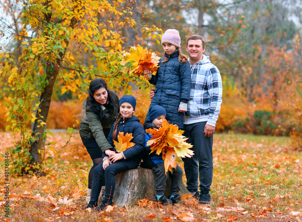 Portrait of a family with children in an autumn city park - happy people posing together near stump, beautiful nature with yellow leaves as background. Portrait of a family with children in an autumn city park - happy people posing together near stump, beautiful nature with yellow leaves as background.