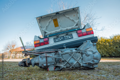 Manual gearbox with overdrive visible outside from a car that is raised up and tilted. Service of a car in the backyard.