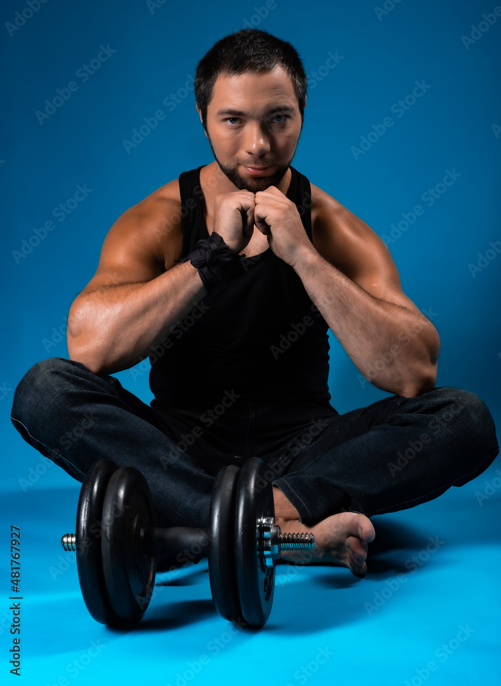 muscular man with dumbbells. sportsman posing in black t-shirt, jeans with dumbbells. studio portrait. blue background muscular man with dumbbells. sportsman posing in black t-shirt, jeans with dumbbells. studio portrait. blue background