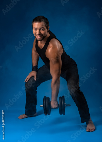 muscular man with dumbbells. sportsman posing in black t-shirt, jeans with dumbbells. studio portrait. blue background