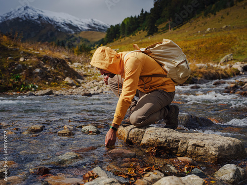 Man drinks clear water from mountain river. Wandering lifestyle, adventure concept autumn vacation outdoors, alone in wild. Travel to North Caucasus, Arkhyz, Russia