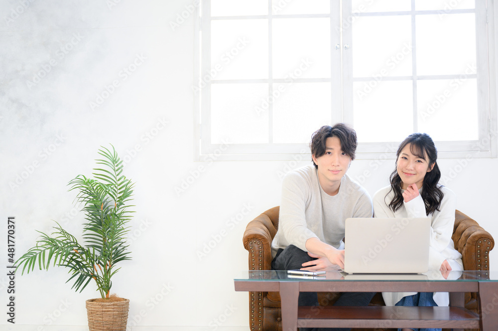 リビングで一緒にパソコンで何かを探してカメラ目線の若いカップル 広角 コピースペース リビングで一緒にパソコンで何かを探してカメラ目線の若いカップル 広角 コピースペース