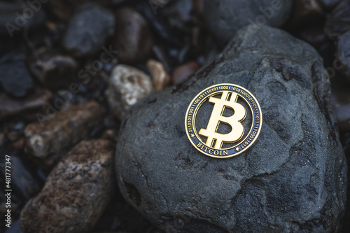 Bitcoin crypto coin with copy space for text. Close-up of single gold Btc cryptocurrency on rocks outdoor. Low key toned photo for banners and news.
