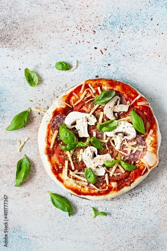 Cooking Italian pizza with tomato sauce, fresh tomatoes, cheese, mushrooms, salami slices and basil . Fresh food cooking concept at home. Semi-finished product, raw dough, step by step cooking. 