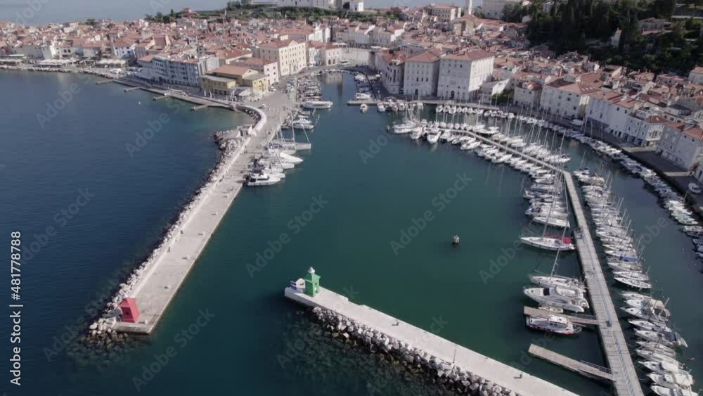 Descriptive panning drone video over the city of Piran in Slovenia, you can see the port with the boats in the water as the main part and the church in the background.