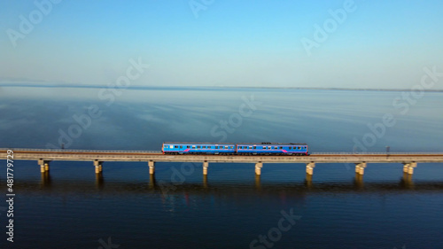 Motion blur of Train is running at high speed on a floating railway bridge. Aerial view of Train look like floating on the lake of Pa Sak Jolasid dam with blue sky at Lopburi province amazing Thailand