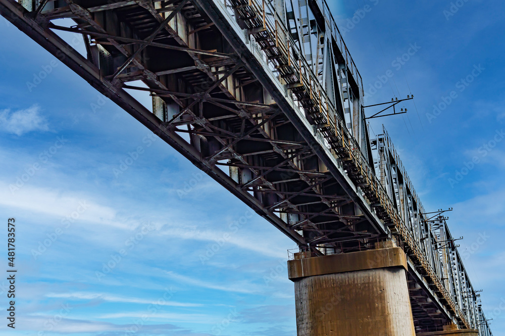 Bottom view of the railway bridge against the blue sky. Railroad bridge. Iranport crossing. Industrial design. Blue sky with white clouds. Railroad tracks. Iron structure on concrete supports.
