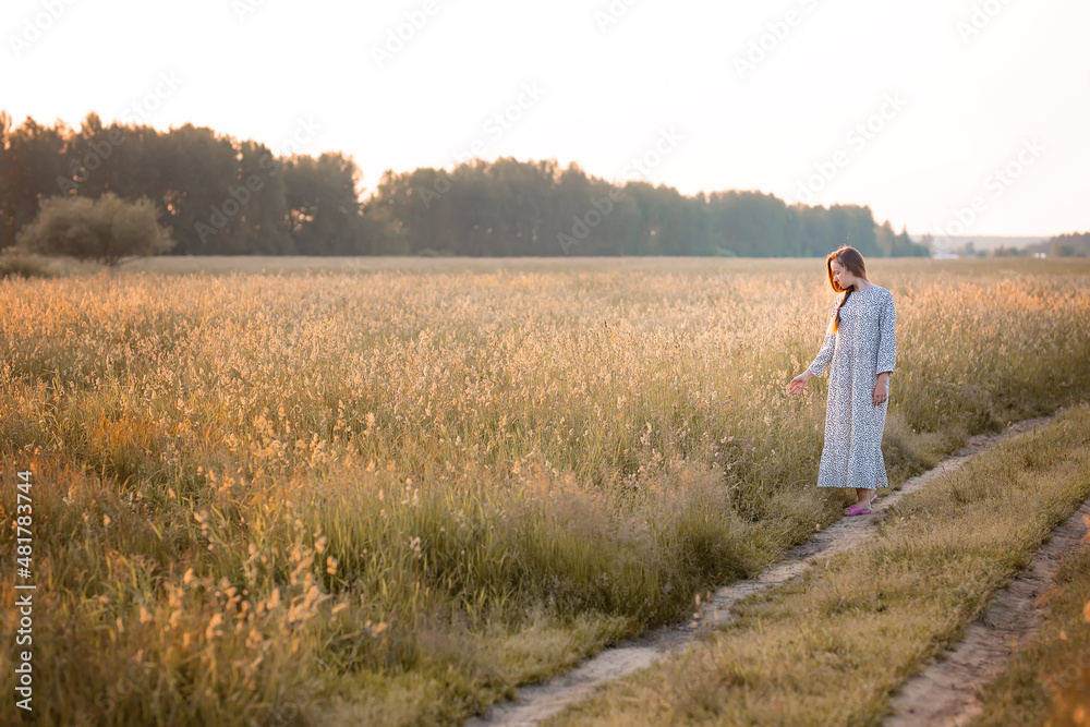 A young woman in a field at sunset. The girl walks across the field in the rays of the sun and touches the grass. The concept of freedom and a rich harvest.