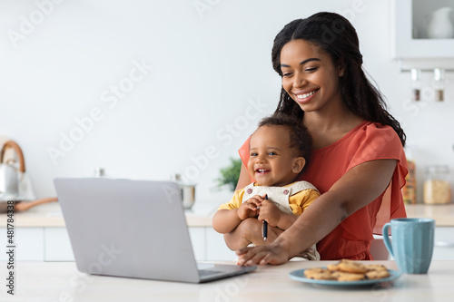 Freelance And Motherhood. Black Woman Holding Baby And Working On Laptop Computer