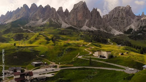 Mutliple vehicles moving over the Sella pass between the beautiful green meadow and high mountains of the dolomites in South-Tirol Italy. Aerial drone liftting view. photo