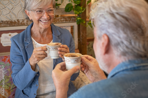 Adult senior couple in coffee shop having breakfast together drinking coffee and cappuccino looking in the eyes. Two attractive smiling elderly people enjoying retirement and stay together.