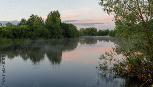 Evening on a river, trees reflection in water. Fog on the forest river