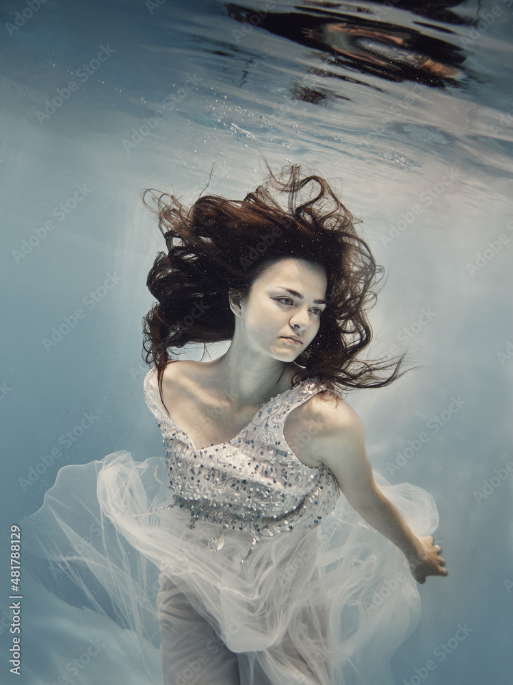 Φωτογραφία A girl in a white dress with dark hair swims underwater as if flying