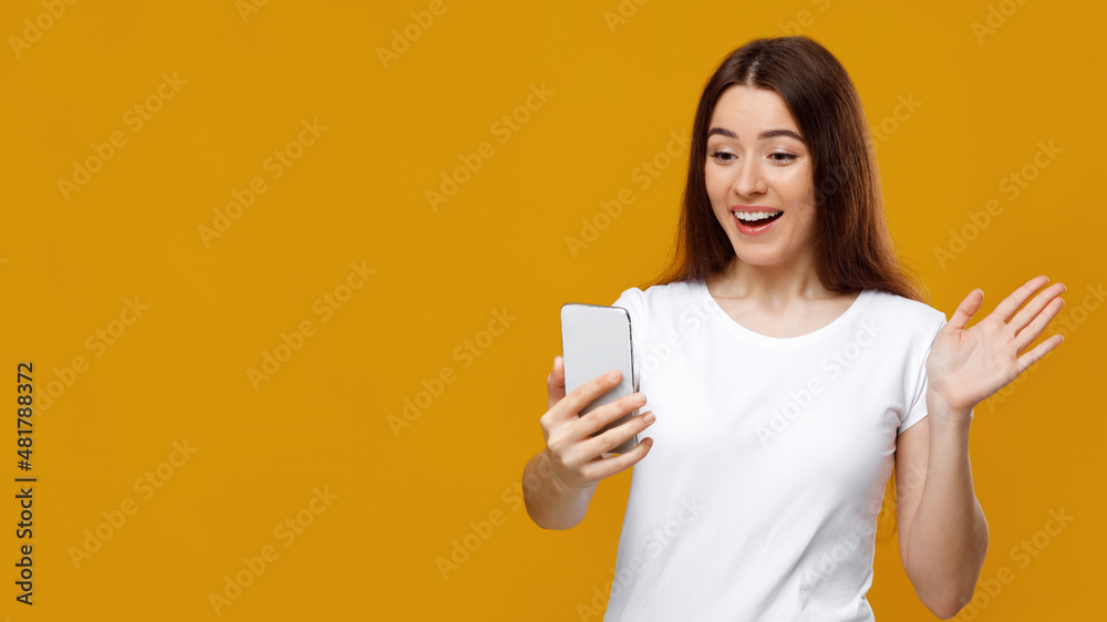 Excited young lady waving at mobile phone screen Excited young lady waving at mobile phone screen