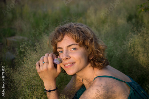 face of a teenage girl sitting in tall grass enjoys nature and relaxation. Nice young woman is resting in the park. spring, summer, sunbathing. dreams, harmony, replenishment of vitality. earth day photo
