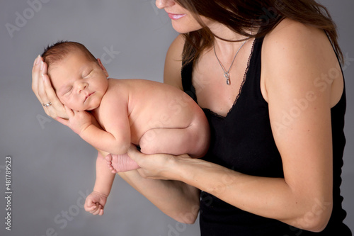 Mother kissing and hugging newborn son at gray background, tender, care, love