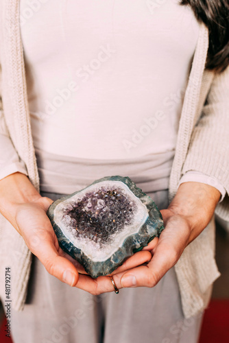 Woman holding amethyst geode indoors. Spiritual unrecognizable woman with a precious mineral on her hand.