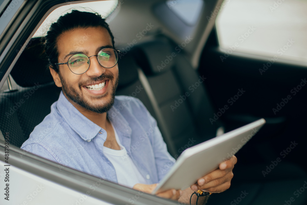 Cheerful indian guy using digital tablet while taking cab