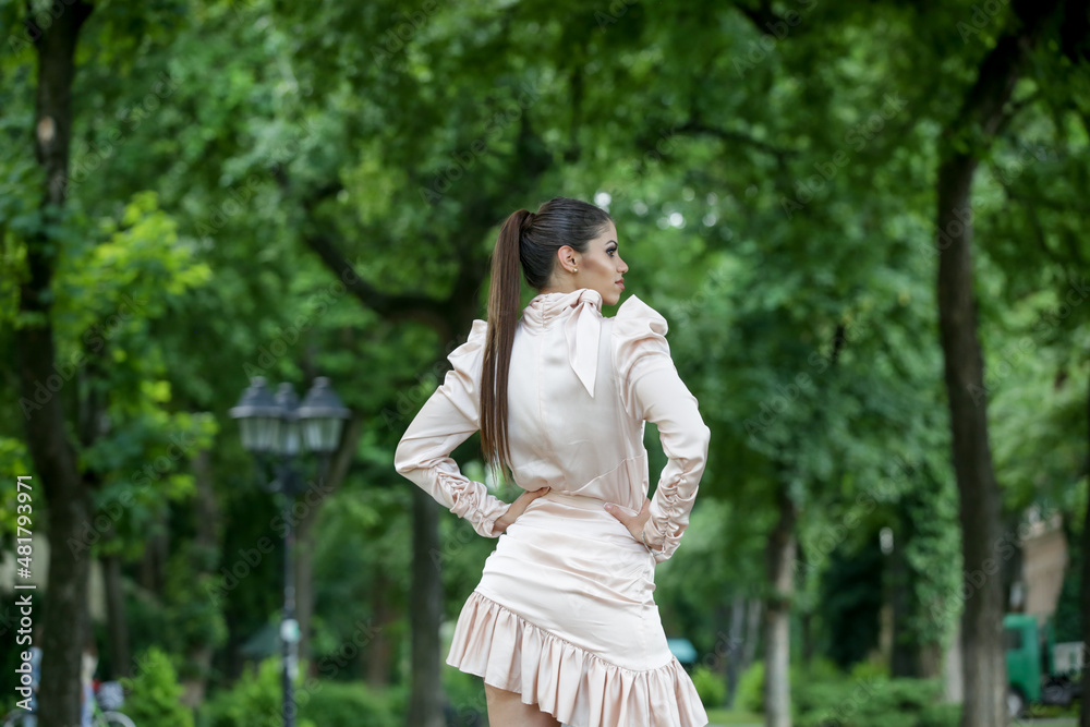 Outdoor portrait of gorgeous young woman with long ponytail in elegant satin dress in city park Outdoor portrait of gorgeous young woman with long ponytail in elegant satin dress in city park