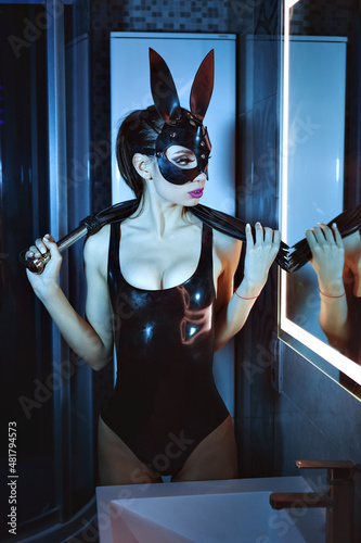 Sexy girl in latex clothes in a bunny mask, in her hands is a leather flogger for BDSM games.