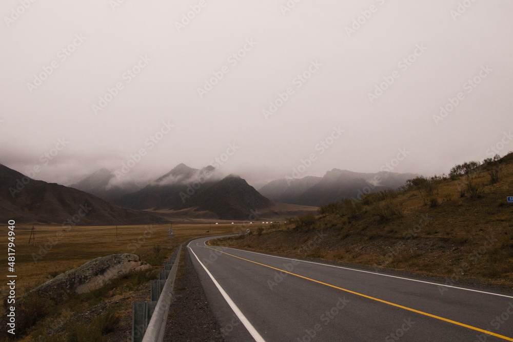 Fototapeta premium Beautiful road in the mountains, late autumn . The peaks of the mountains are covered with fog. Altai.