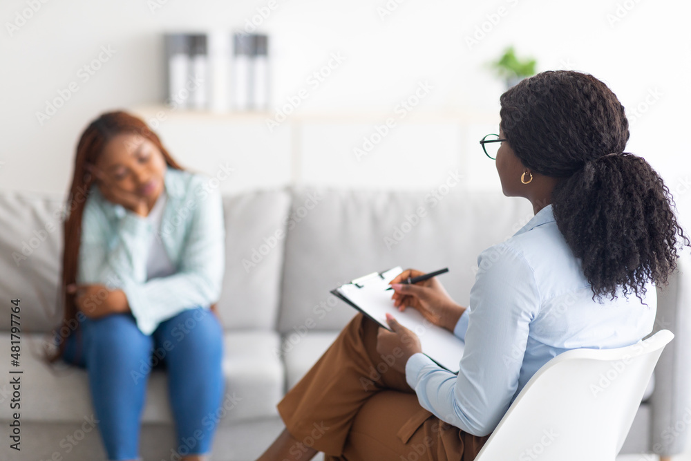 Depressed black lady receiving professional psychological help at mental clinic, selective focus Depressed black lady receiving professional psychological help at mental clinic, selective focus