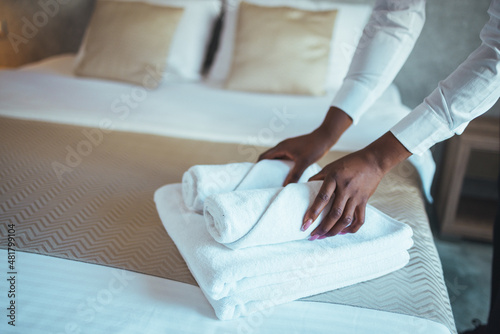 Young hotel maid making the bed with clean fresh towels. Hands of hotel maid bringing fresh towels to the room. Close up of a young hotel maid holding clean folded towels