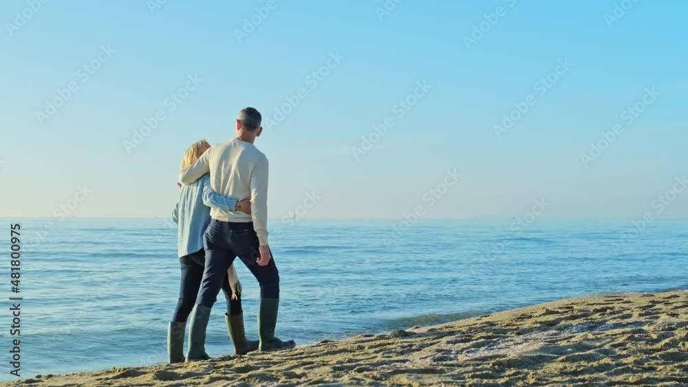 Mature couple walking on the beach with arms around Mature couple walking on the beach with arms around