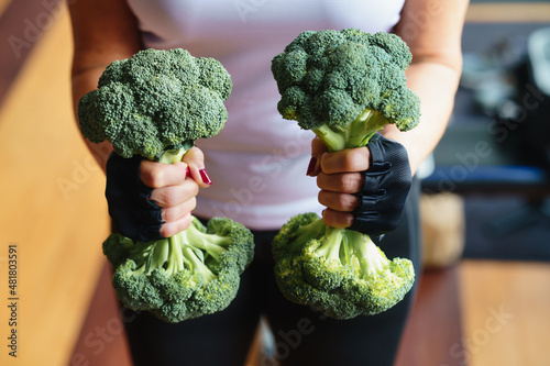 Woman in the gym lifts a broccoli in the form of a dumbbell