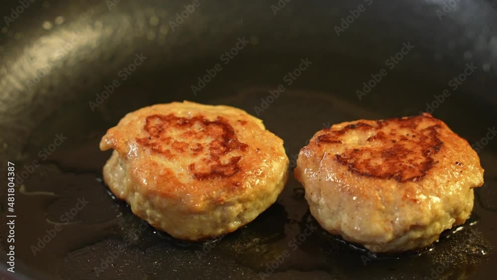 Two chicken cutlets are fried in a black frying pan in olive oil Two chicken cutlets are fried in a black frying pan in olive oil