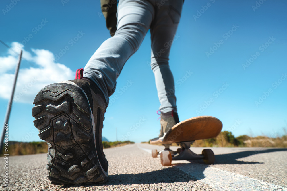 From below, anonymous man with black shoes standing on a skateboard on an asphalt road with straight line signs. positivity effect. From below, anonymous man with black shoes standing on a skateboard on an asphalt road with straight line signs. positivity effect.