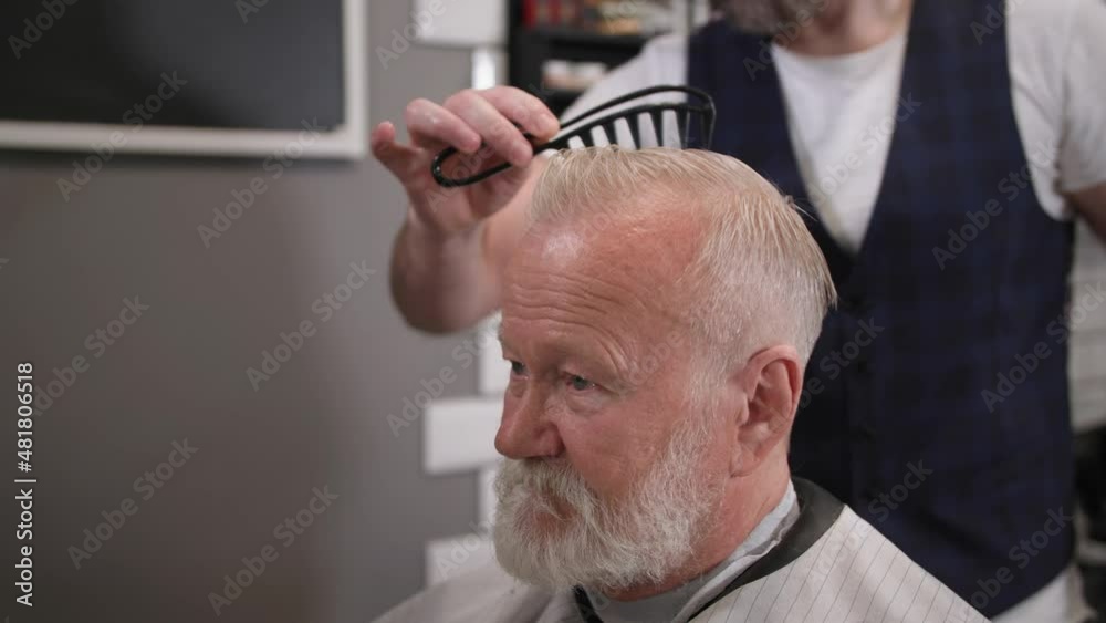 professional barber does hair styling with a comb to a stylish cheesy male client with a hairdressing salon