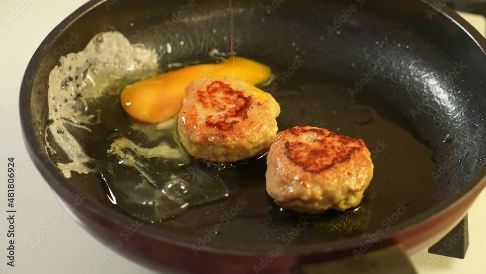 Two chicken cutlets are fried with eggs in olive oil in a black Teflon pan. Slow motion Two chicken cutlets are fried with eggs in olive oil in a black Teflon pan. Slow motion