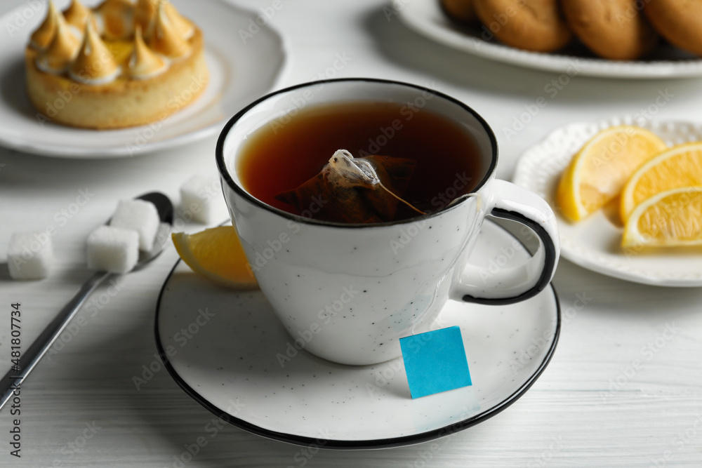 Tea bag in cup of hot water and lemon on white wooden table