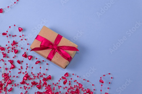 flat lay of gift with red bow next to beads with hearts on very peri color background. holiday concept, congratulations, valentine's day, engagement, wedding, anniversary. top view. copy space photo