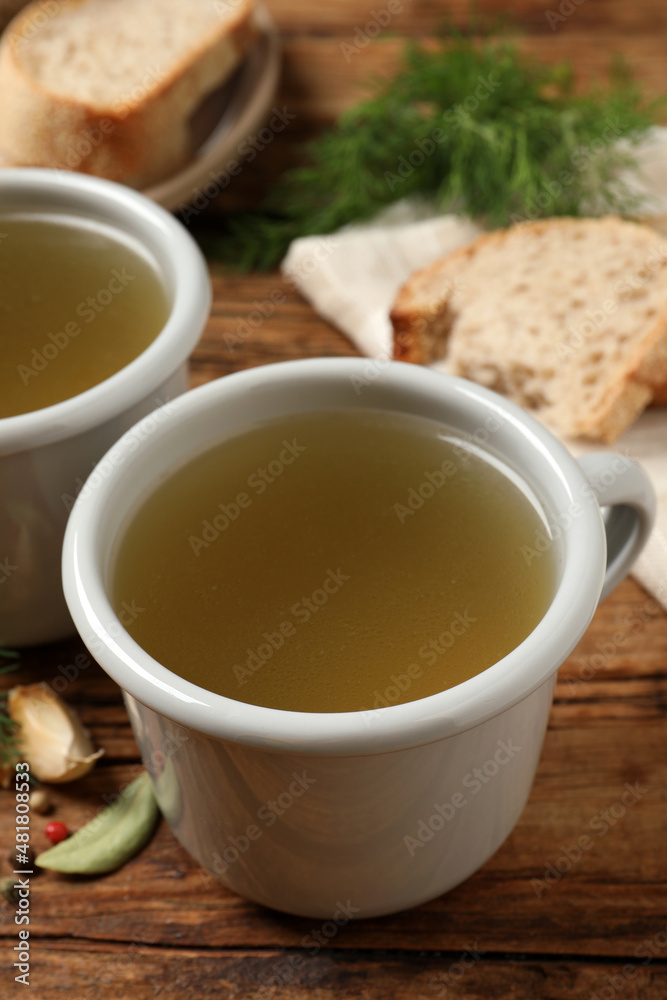 Hot delicious bouillon in cups on wooden table, closeup Hot delicious bouillon in cups on wooden table, closeup
