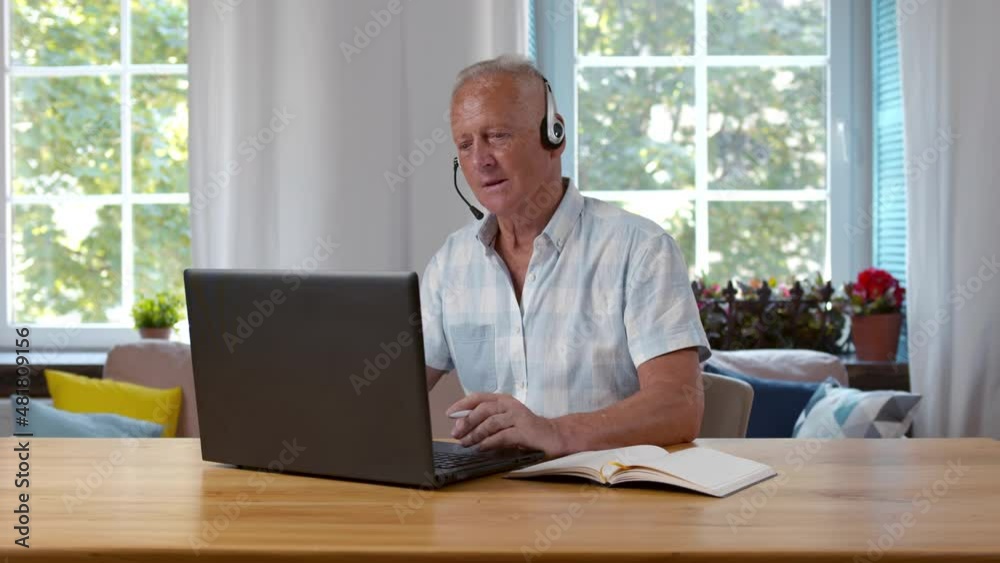 Senior man in headphones having video conference and writing notes. Realtime. Senior man in headphones having video conference and writing notes. Realtime.