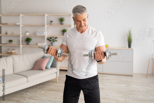 Workout during lockdown. Athletic middle-aged man doing dumbbell workout at home, training in living room photo