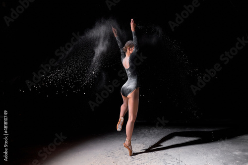Flexible ballet dancer woman dancing and sprinkle flour on black background, attractive slim slender lady in black bodysuit in slow motion, moving gracefully. full-length portrait, side view