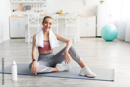 Satisfied european pretty young blonde fitness blogger resting after workout at home with water