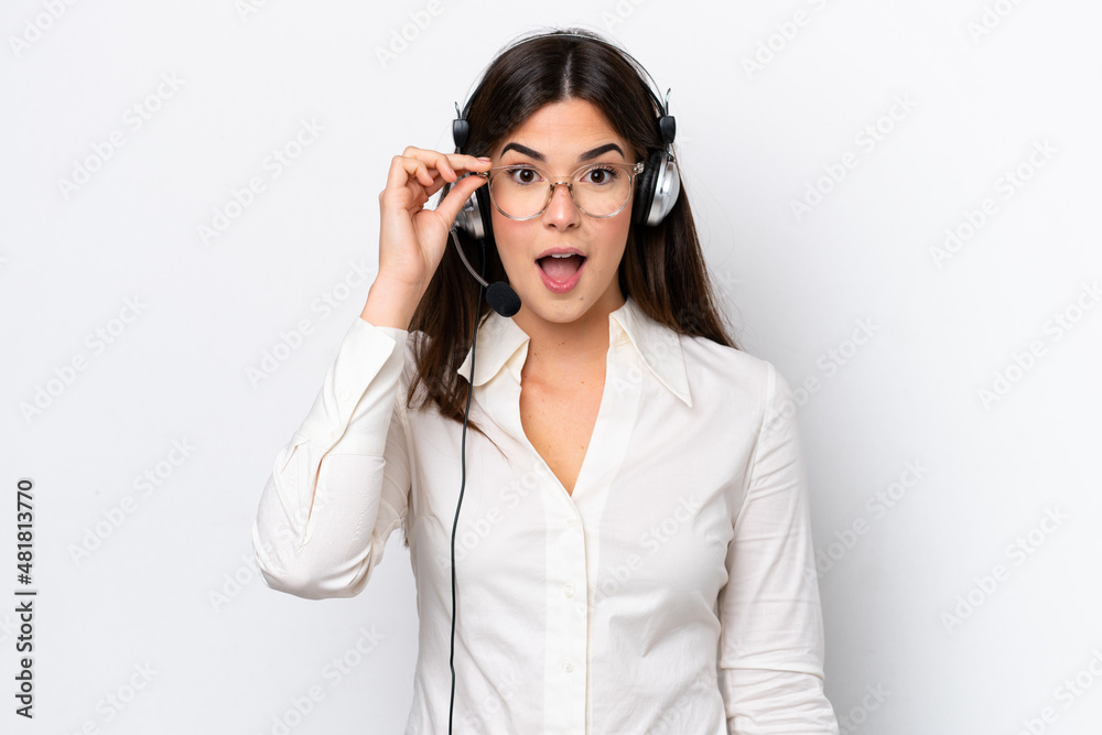 Telemarketer caucasian woman working with a headset isolated on white background with glasses and surprised