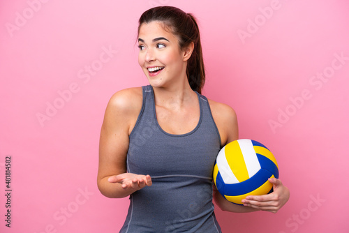 Young Brazilian woman playing volleyball isolated on pink background with surprise expression while looking side