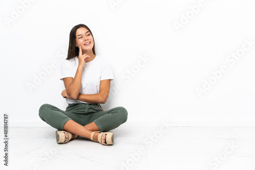 Teenager girl sitting on the floor thinking an idea while looking up